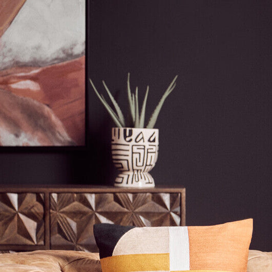 Brown leather sofa with colorful pillows against a dark wall.
