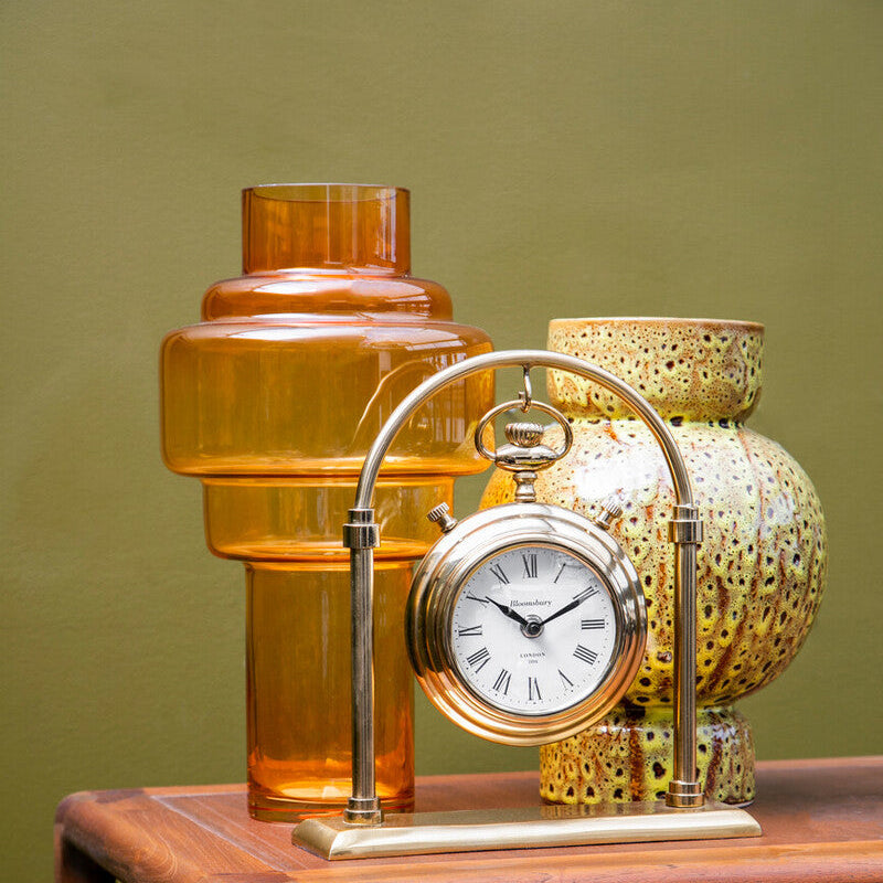 Decorative clock with amber glass lamp and textured gold lamp on a wooden surface against a green wall.