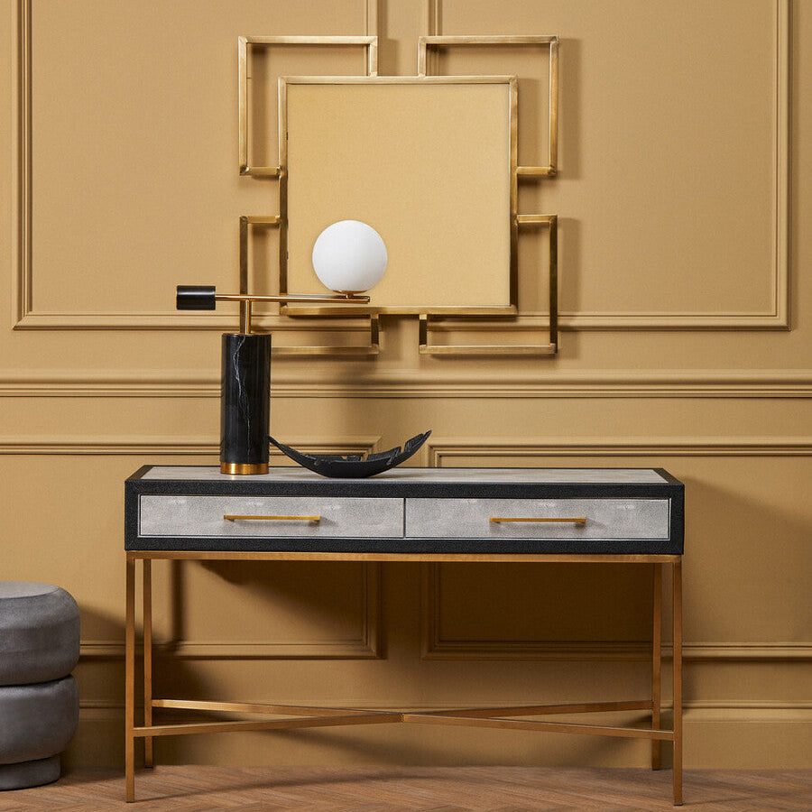 Decorative console table with a lamp and mirror against a beige wall.