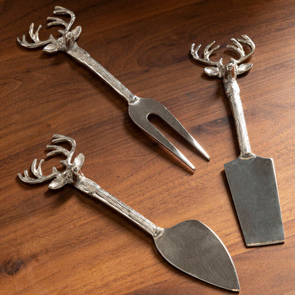 Three metal utensils with deer head designs on a wooden surface