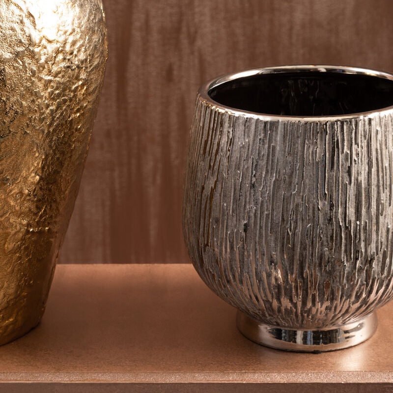 Silver textured cup on a wooden shelf with a gold decorative object in the background