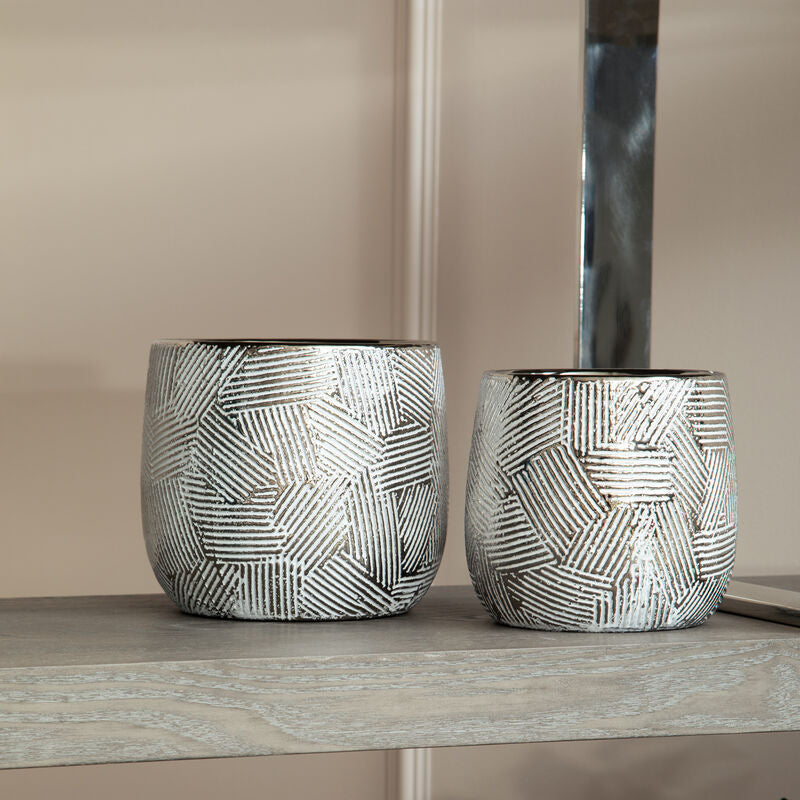 Two decorative pots with geometric patterns on a reflective surface.