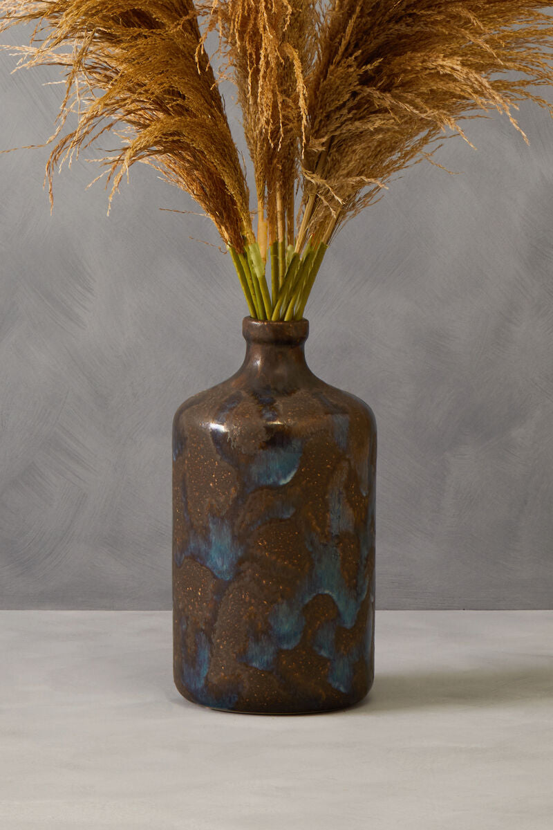 Brown ceramic vase with blue glaze holding dried pampas grass against a gray background