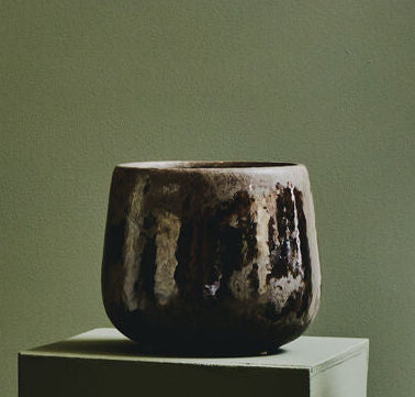 Three dark ceramic vases on a light green surface with a green and white background