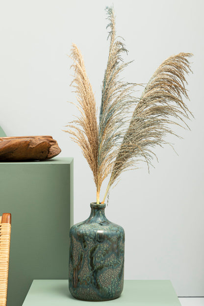 Decorative vase with dried pampas grass on a light green surface against a white wall