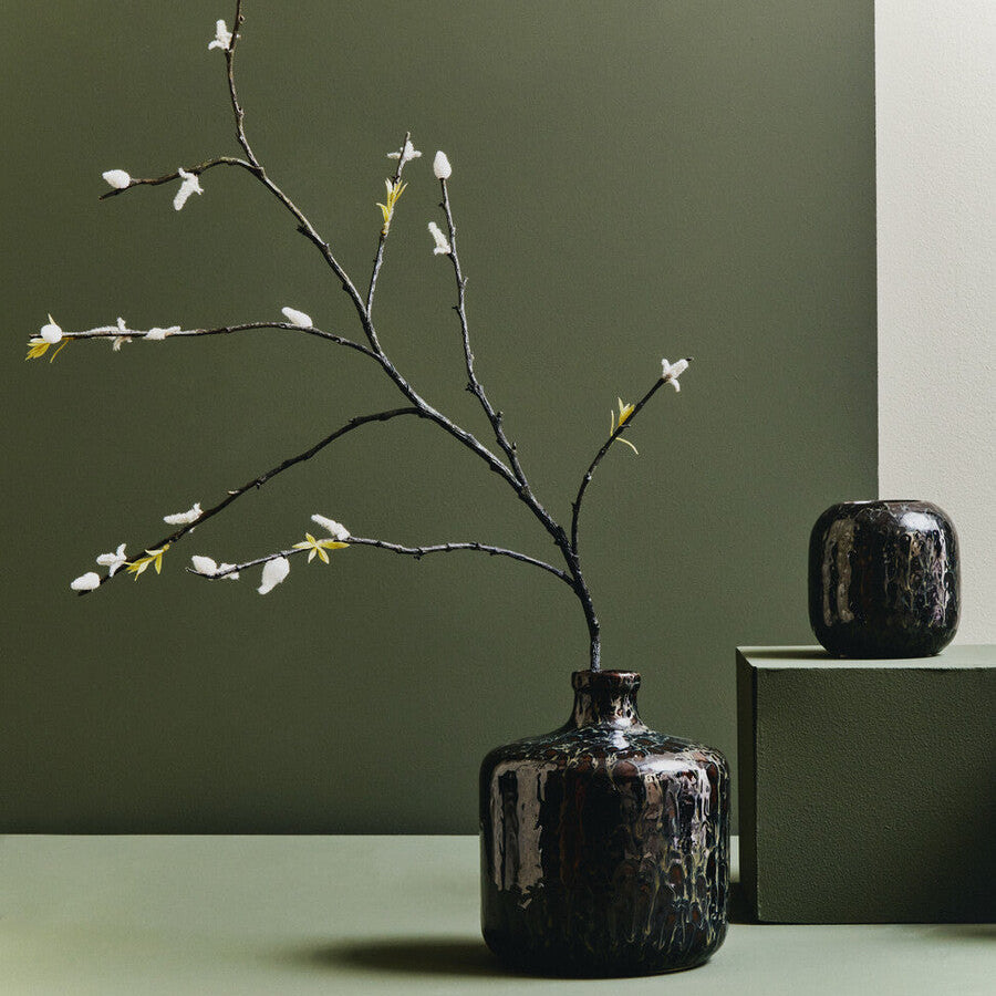 Dark brown vase with branches on a green surface against a green wall