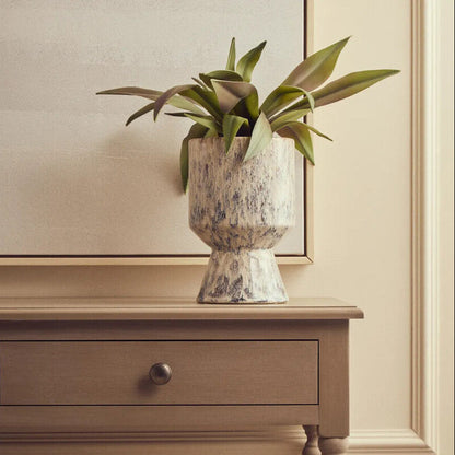 Decorative vase with green plant on a wooden side table against a neutral wall.