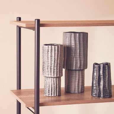 Three metallic vases on a wooden shelf against a beige wall