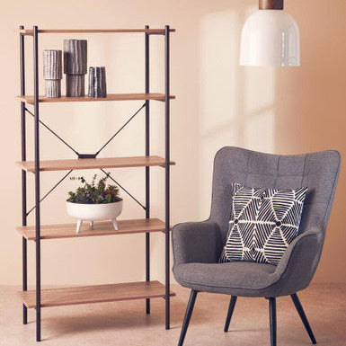 Gray armchair with a patterned pillow next to a wooden shelf against a beige wall.