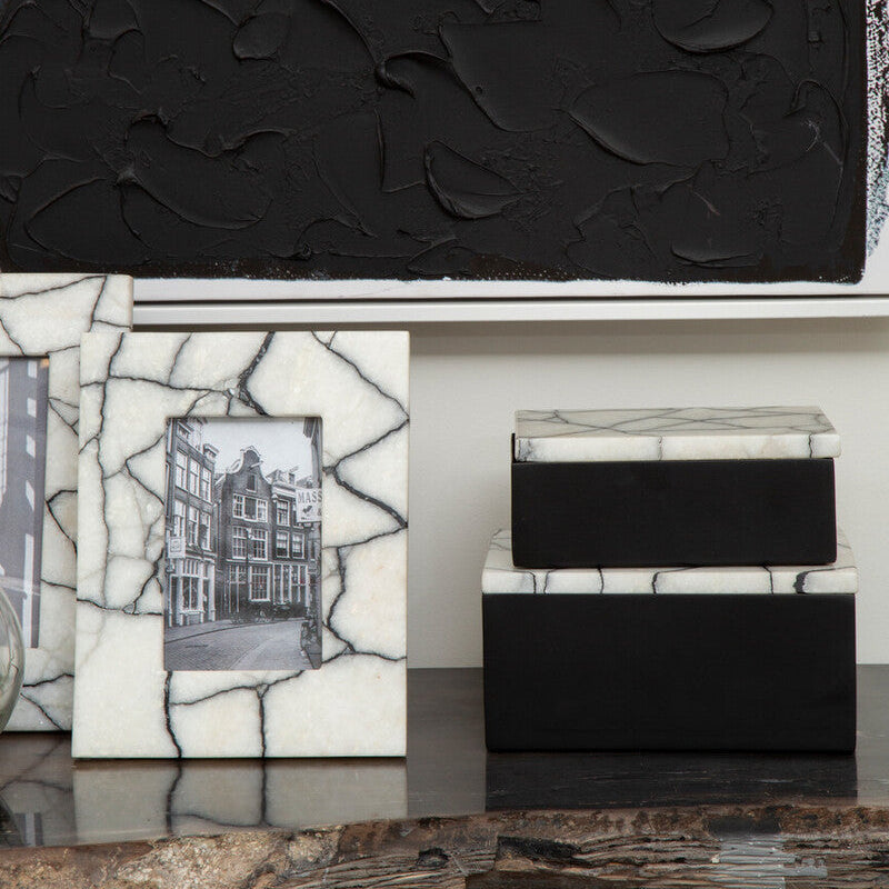 Decorative items including a black textured box, a white mosaic box, and a black and white photo frame on a reflective surface.