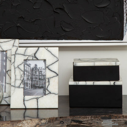 Decorative items including a black textured box, a white mosaic box, and a black and white photo frame on a reflective surface.
