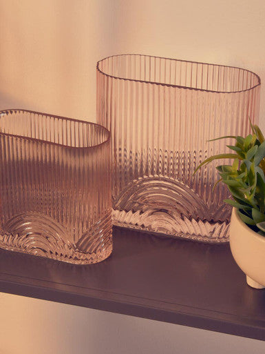 Two ribbed glass vases on a shelf with a plant in the background