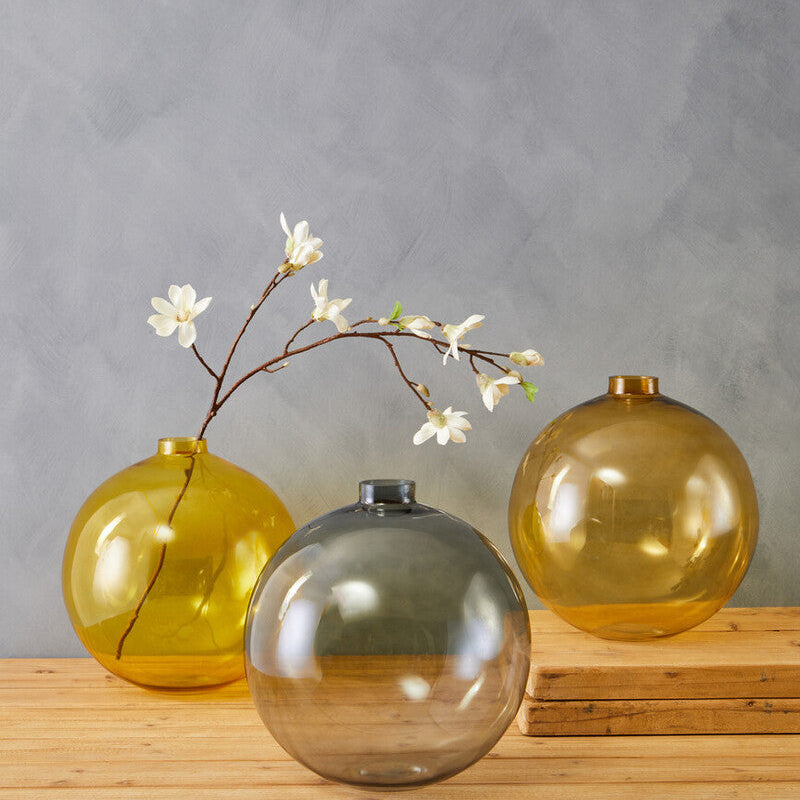 Three glass vases of different colors on a wooden surface with a gray background