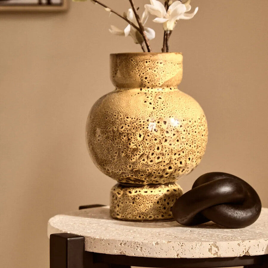 Decorative vase with textured surface on a table against a beige wall