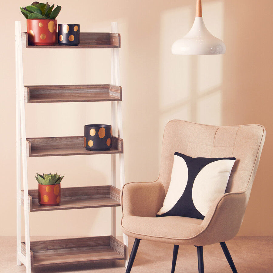 Beige armchair with a decorative pillow next to a wooden shelf with plants and decor items.