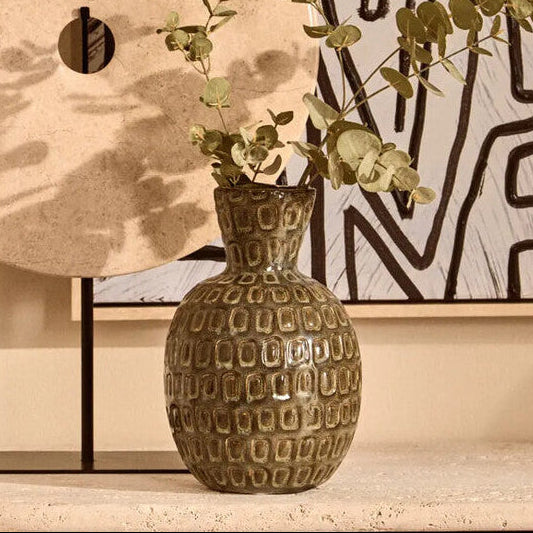 Decorative vase with textured pattern and greenery on a shelf against a wall with abstract art.