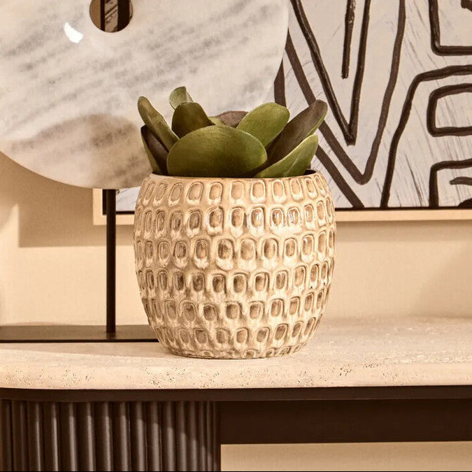 Decorative scene with a textured vase, marble orb, and abstract art on a wall.
