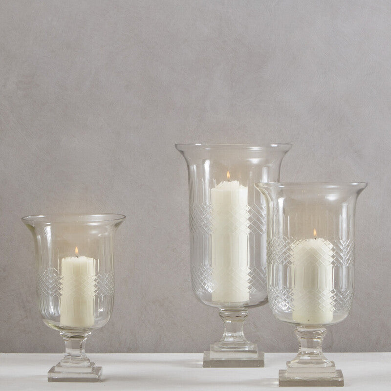 Three glass candle holders with candles on a white surface against a gray background