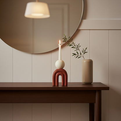 Decorative items on a wooden table with a round mirror above, against a beige wall.