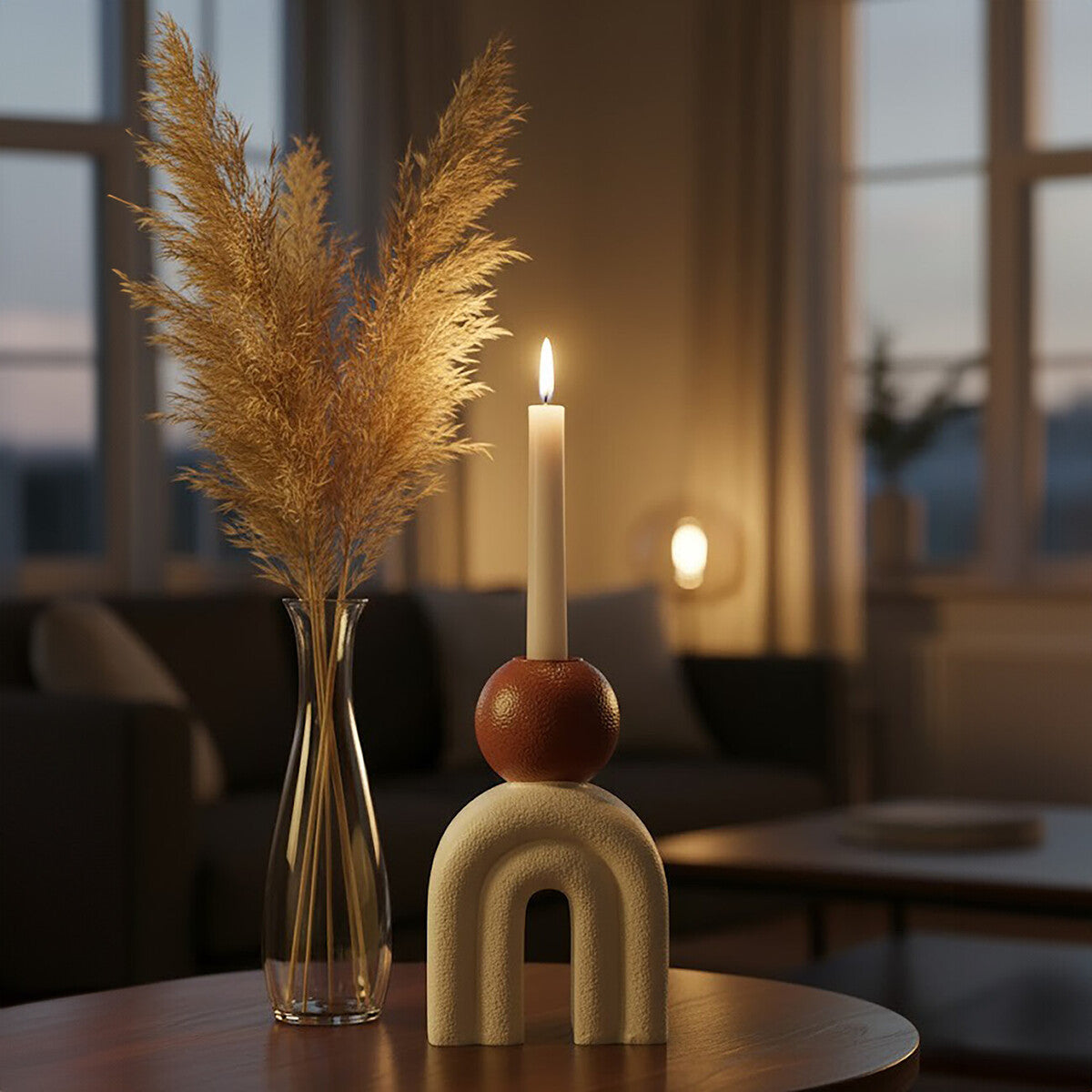 Decorative candle with a vase of dried pampas grass on a table in a softly lit room.
