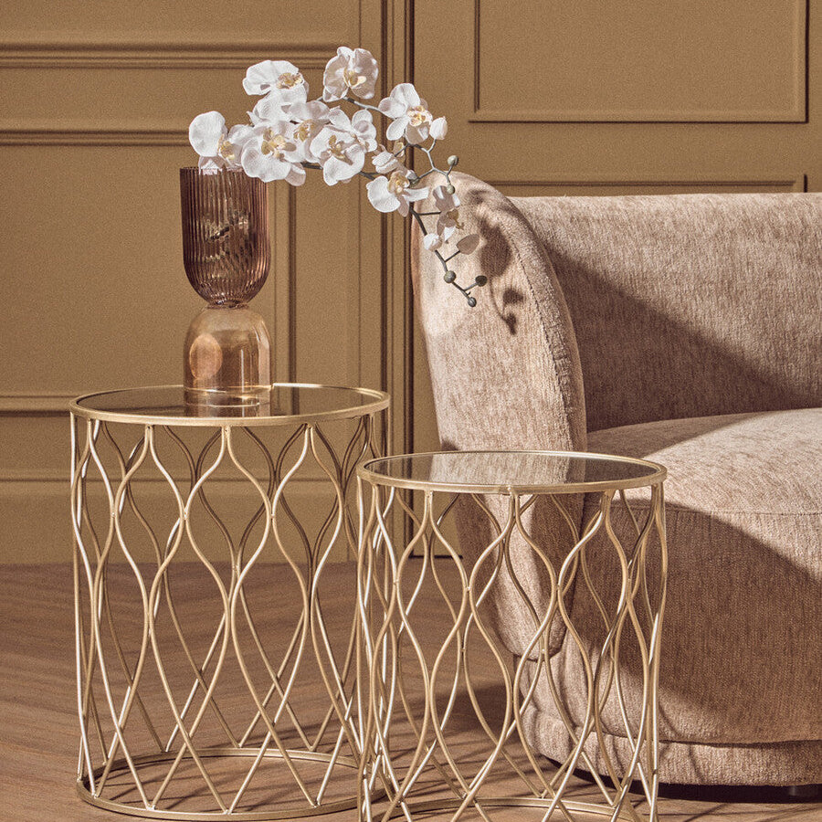 Gold side tables with a vase and flowers on a wooden floor against a beige wall.