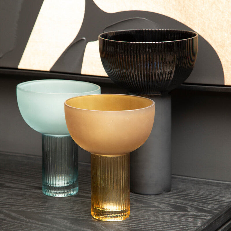Three glass bowls in different colors on a dark surface with abstract wall art in the background.
