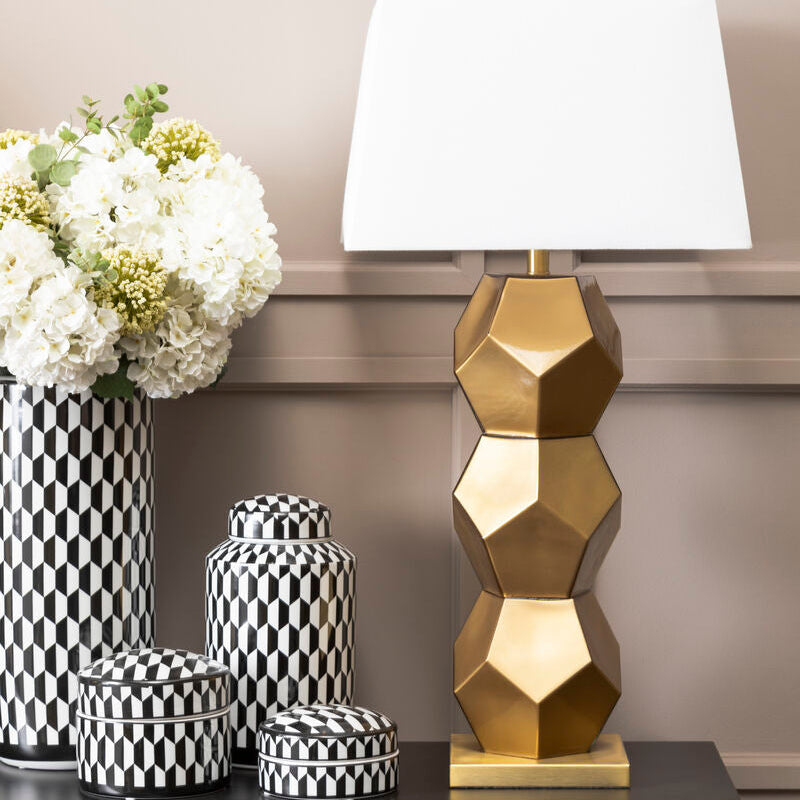 Decorative table with gold lamp, black and white vases, and flowers against a neutral wall.