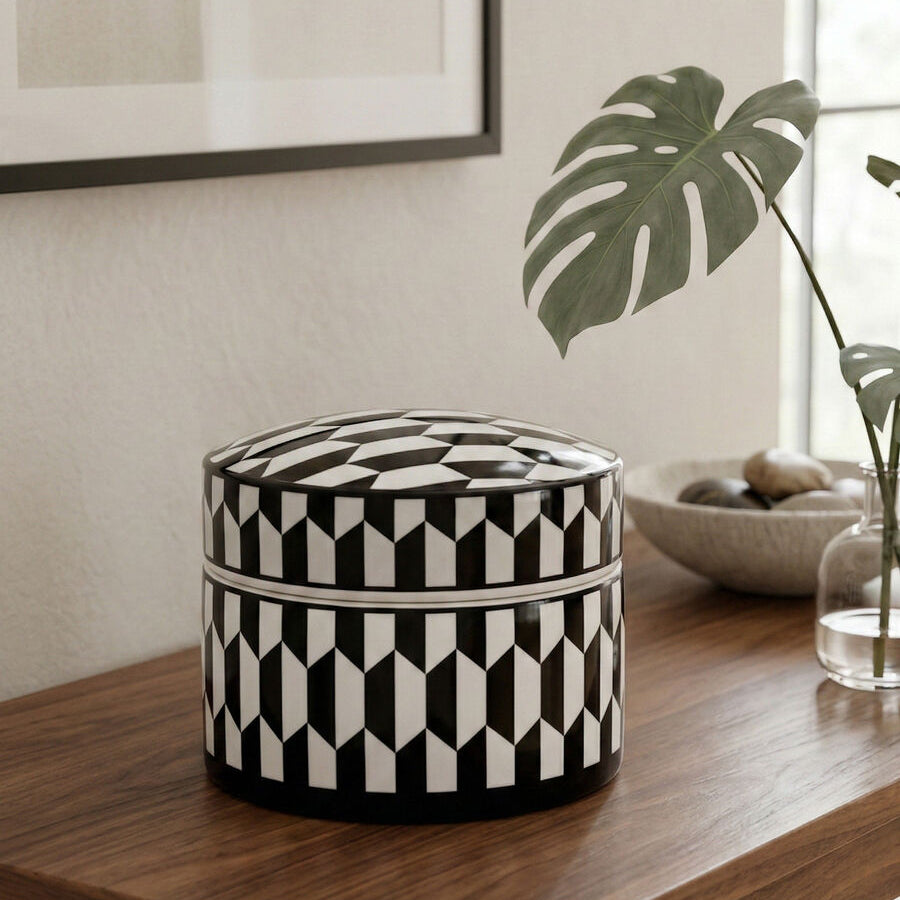 Black and white patterned ottoman on a wooden table with a plant and abstract art in the background.
