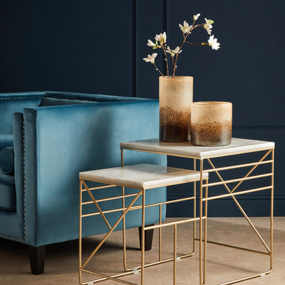 Gold side table with marble top next to a blue armchair against a dark wall.