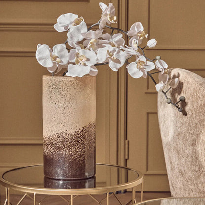Decorative vase with white flowers on a glass table against a beige wall.