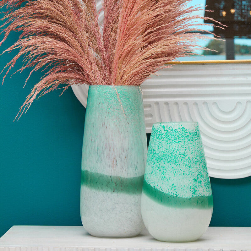 Decorative vases with pink dried grass against a teal wall