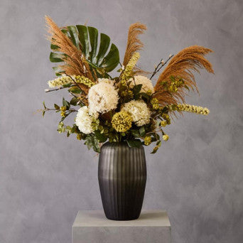 Floral arrangement in a black vase on a gray pedestal against a gray background