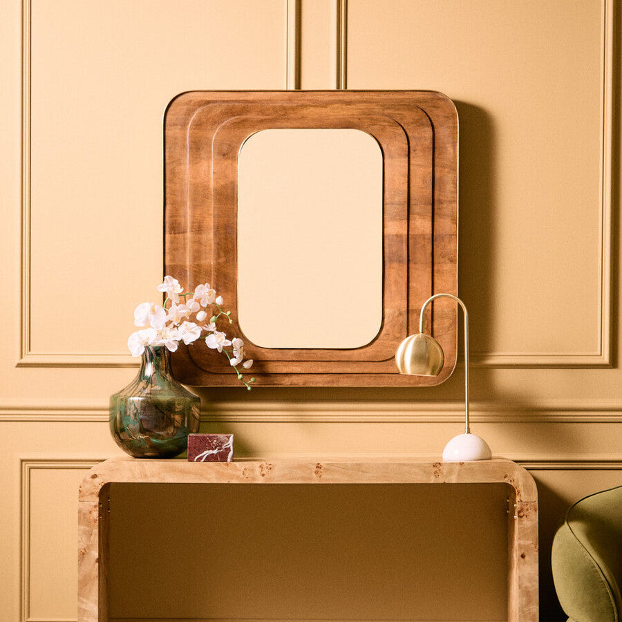 Wooden console table with mirror and decorative items against a beige wall.