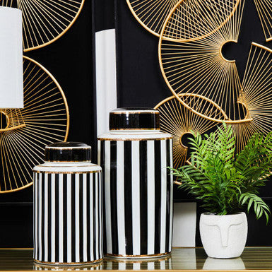 Decorative vases with black and white stripes on a table with a geometric gold design in the background.