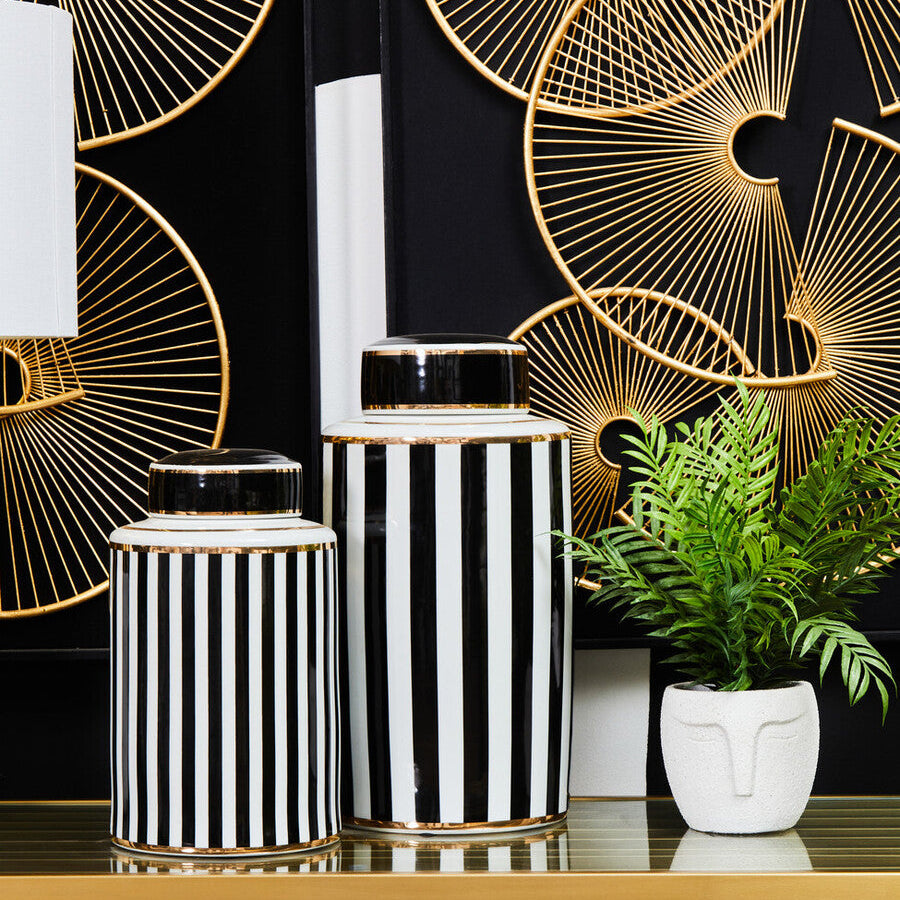 Decorative vases with black and white stripes on a table with a geometric gold design in the background.