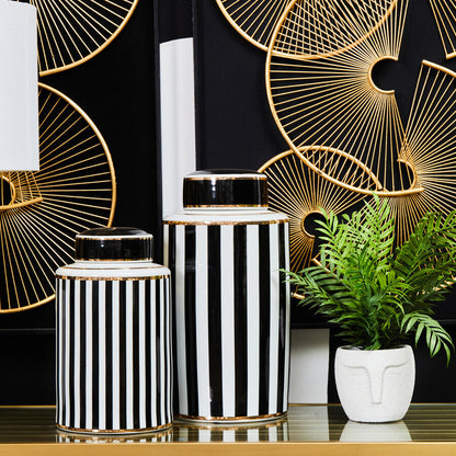 Decorative vases with black and white stripes on a table with a geometric gold design in the background.