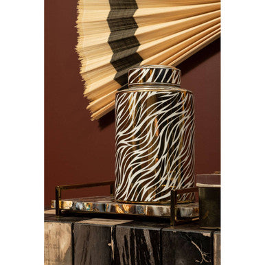 Decorative zebra-patterned vase on a reflective surface with a fan in the background