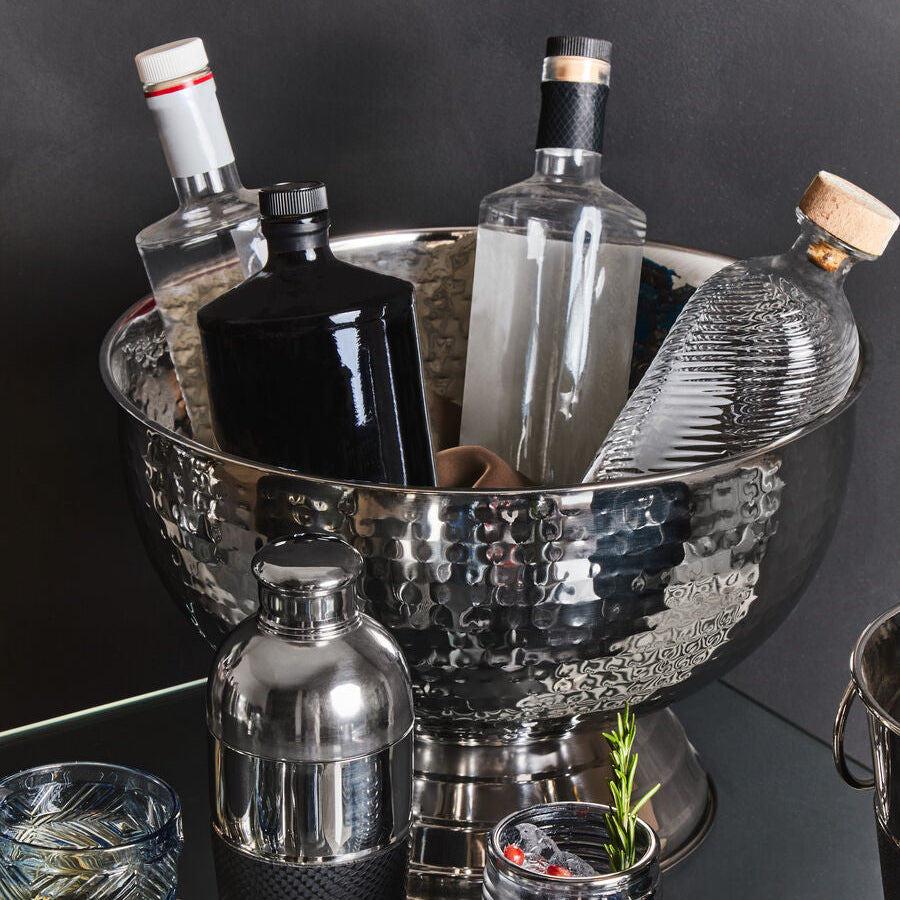 Bar setup with bottles, a cocktail shaker, and glasses on a dark surface.