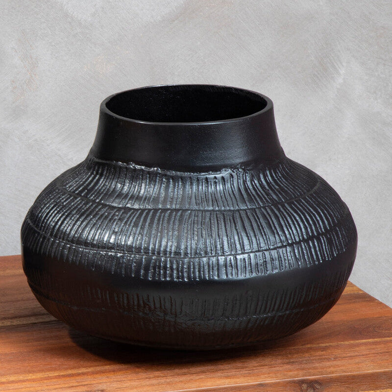 Black textured vase on a wooden surface with a gray background