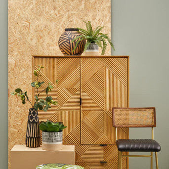 Wooden cabinet with decorative items, plants, and a bar stool in a room setting.