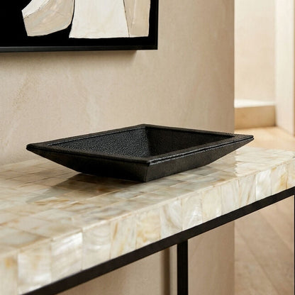Black textured rectangular bowl on a marble surface with abstract art in the background
