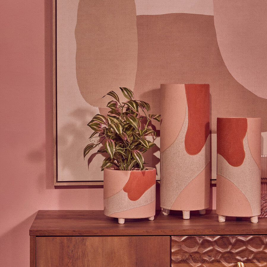 Decorative vases with abstract patterns on a wooden cabinet against a pink wall with abstract art.
