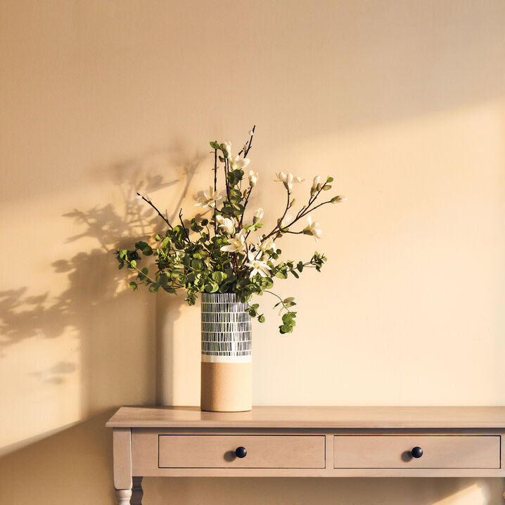 Wooden console table with a vase of flowers and a woven basket against a beige wall.