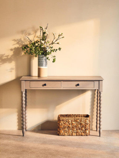 Wooden console table with a vase of flowers and a woven basket against a beige wall.