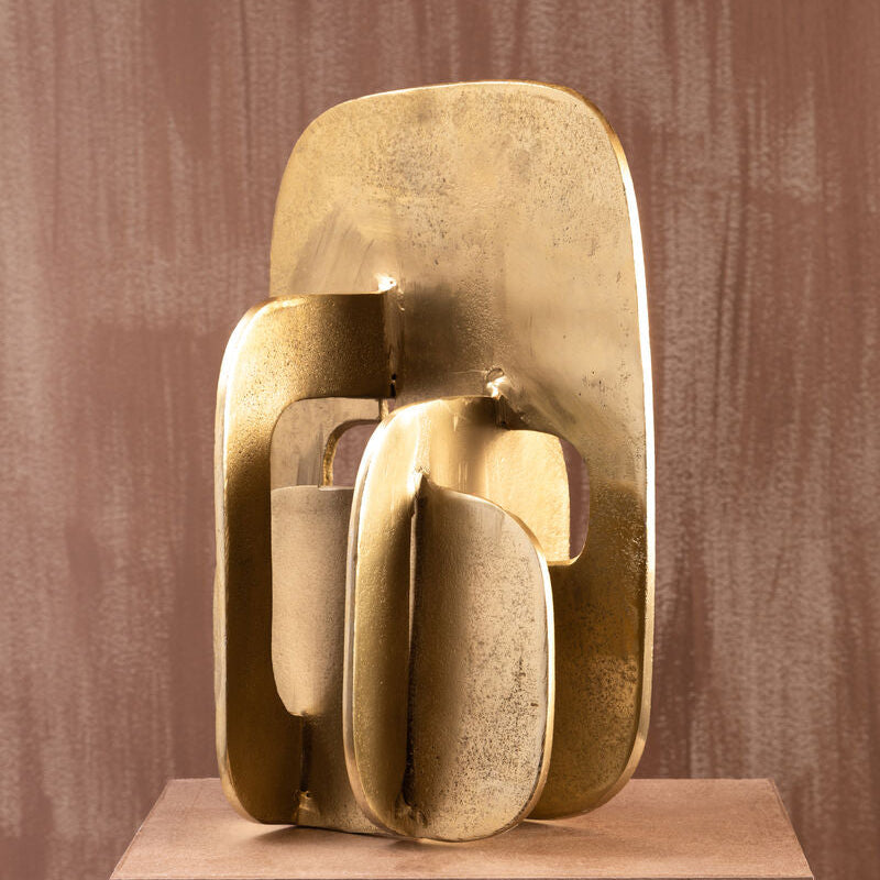Gold abstract sculpture on a brown pedestal against a textured brown wall