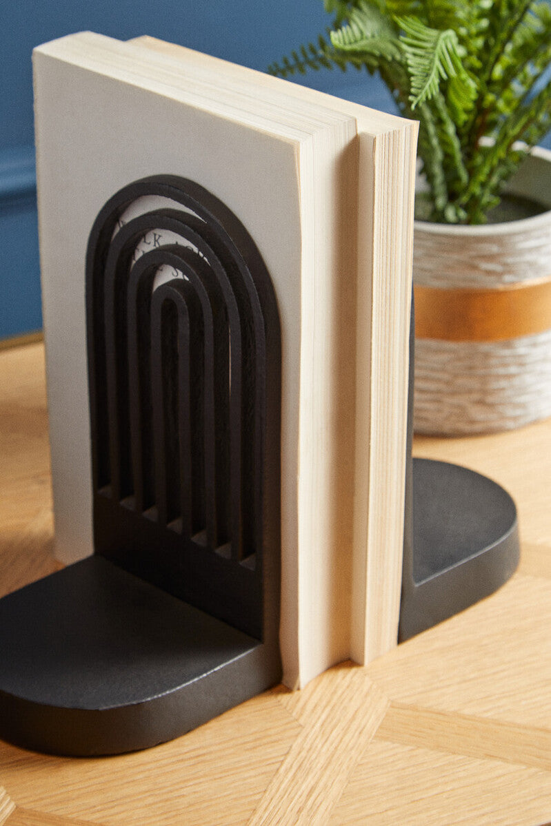 Black arch-shaped bookend on a wooden surface with a plant in the background