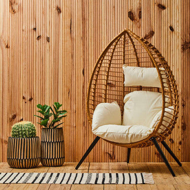 Wicker egg chair with white cushions against a wooden wall.