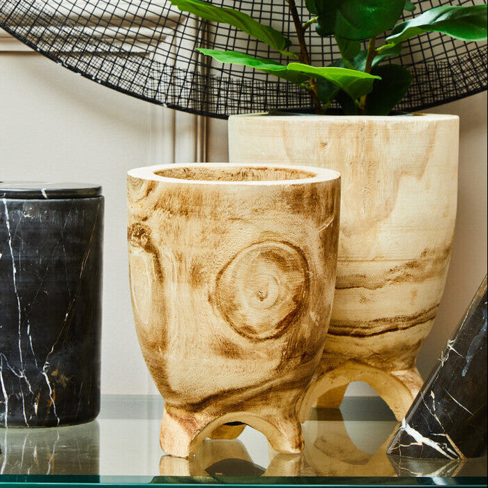 Decorative items including a black marble candle holder, wooden vase, and plant on a reflective surface.