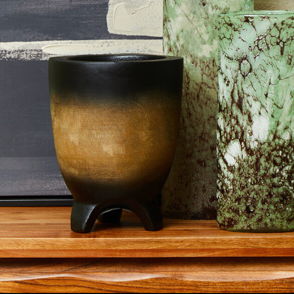 Three ceramic vases on a wooden surface with a striped wall in the background