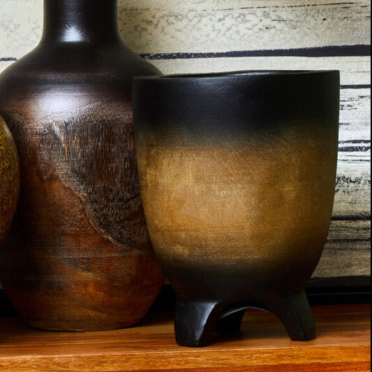 Three ceramic vases on a wooden surface with a striped wall in the background